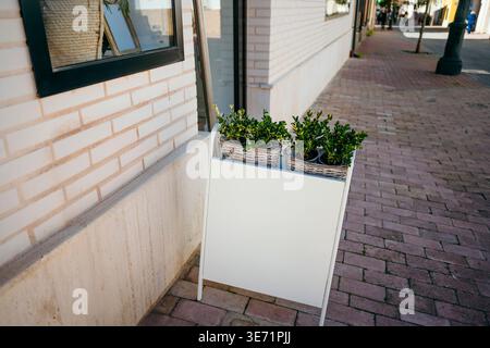 Leeres weißes Sandwichbrett-Schild, das auf einem Bürgersteig neben einer Gebäudewand steht Stockfoto