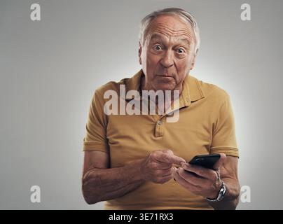 Porträt, Schock und alter Mann mit Telefon im Studio, Online-Benachrichtigung und Verkaufsalarm für Kommunikation. Nachrichten, Zeiger oder leitende Person mit Überraschung Stockfoto