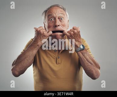 Lustiges Gesicht, Mund und Porträt eines alten Mannes im Studio für Comedy, Humor oder verspielten Charakter. Gesichtsausdruck, dumm und albern mit einer Seniorin Stockfoto