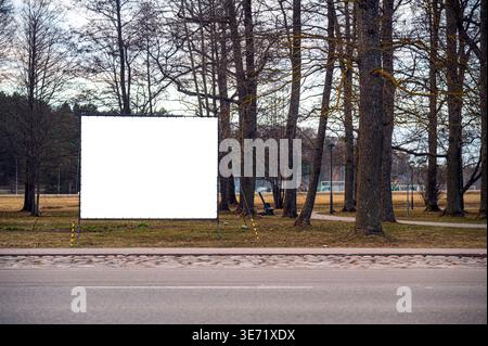 Eine leere Vorlage steht an einem sonnigen Tag zwischen Bäumen in einem Park neben einer Straße. Stockfoto