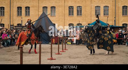 BERLIN, DEUTSCHLAND - 5. APRIL 2026: Ein berittener Künstler in roter Tracht nähert sich einem gegnerischen Ritter auf einem weißen Pferd während eines mittelalterlichen Turniers Stockfoto