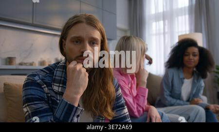 Verärgerter, besorgter kaukasischer Mann, der zu Hause denkt und sich einsam ängstlich fühlt, schließt introvertierte Männer aus, die Stress leiden und Freunde ignorieren, während multiethnische Frauen Stockfoto