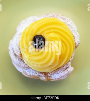 Zeppole di San Giuseppe, traditionelles italienisches Choux-Gebäck mit weichem Ring, einem Schuss Vanillecreme und einer dunklen schwarzen Kirsche auf der Oberseite, die mit Puderzucker für die Feier des St. Josephs-Tages bestäubt ist Stockfoto