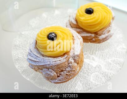 Zeppole di San Giuseppe, traditionelles italienisches Choux-Gebäck mit weichem Ring, einem Schuss Vanillecreme und einer dunklen schwarzen Kirsche auf der Oberseite, die mit Puderzucker für die Feier des St. Josephs-Tages bestäubt ist Stockfoto