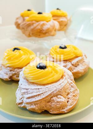 Zeppole di San Giuseppe, traditionelles italienisches Choux-Gebäck mit weichem Ring, einem Schuss Vanillecreme und einer dunklen schwarzen Kirsche auf der Oberseite, die mit Puderzucker für die Feier des St. Josephs-Tages bestäubt ist Stockfoto
