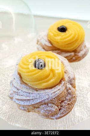 Zeppole di San Giuseppe, traditionelles italienisches Choux-Gebäck mit weichem Ring, einem Schuss Vanillecreme und einer dunklen schwarzen Kirsche auf der Oberseite, die mit Puderzucker für die Feier des St. Josephs-Tages bestäubt ist Stockfoto
