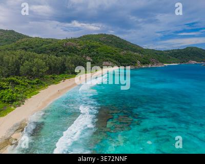 Aus der Vogelperspektive auf die türkisfarbenen Wellen, die sanft den unberührten Sand unter den grünen Hängen von Mahe Island, Police Bay, Mahe Island, Seychellen küssen. Stockfoto