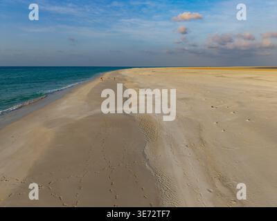Aus der Vogelperspektive auf türkisfarbene Wellen, die den goldenen Sand der Lagune von Qalanciya unter einem ruhigen Himmel küssen, Qalanciya, Socotra, Jemen. Stockfoto