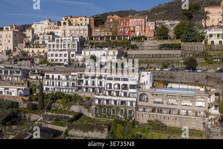 Aus der Vogelperspektive auf sonnenverwöhnte Gebäude kaskadieren den Hang hinunter, mit leuchtenden Farben, die sich von dem üppigen Grün abheben, Ravello, Salerno, Italien Stockfoto