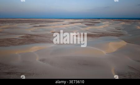 Aus der Vogelperspektive glatte windgeformte Sanddünen und Flachflächen unter weichem Dämmerungshimmel, minimaler Wüstenlandschaft mit sanften Kurven und fernem Horizont. Zah Stockfoto