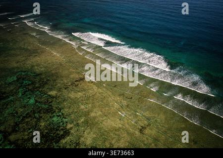 Aus der Vogelperspektive der türkisfarbenen Wellen, die sanft die Küste küssen, erzeugen einen faszinierenden Tanz aus Licht und Schatten an der Küste, Paje, Tansania. Stockfoto