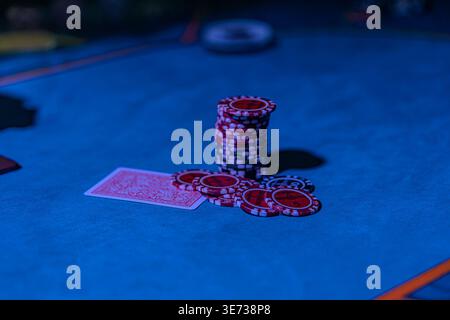 Nahaufnahme eines Blackjack-Spiels in einem schwach beleuchteten Kasino mit dunkelblauem Filztisch, rot-weißen Spielkarten und Chips mit geringer Schärfentiefe Stockfoto