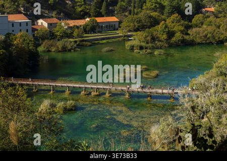 Traditionelle Häuser an einem klaren türkisfarbenen Fluss, umgeben von üppig grünen Wäldern. Friedliche ländliche Landschaft in natürlicher Umgebung. Stockfoto