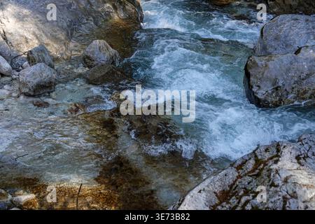 Klarer Alpenbach, der über Felsen fließt, und Sonnenlicht reflektiert auf türkisfarbenem Wasser in Ramsau, Berchtesgadener Land, Bayern Stockfoto