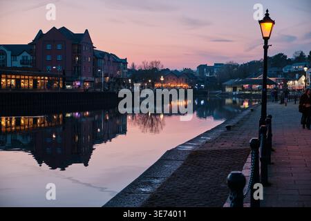 Exeter, Vereinigtes Königreich - 20. März 2026. Eine viktorianische Gaslampe leuchtet am Ufer des Kais, während ein leuchtender rosafarbener und goldener Sonnenuntergang den Fluss exe erleuchtet Stockfoto