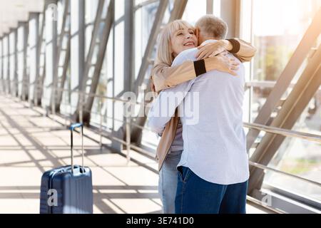 Ältere Ehepaare teilen sich eine warme Umarmung im hellen, sonnendurchfluteten Flughafenkorridor Stockfoto
