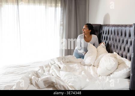 Vertikales Video: Reaktion auf Sonne, indische Frau macht Bett im Schlafzimmer, trägt graue Pjs, Kopierraum. Kissen, Federdecke, Bettwäsche, Bettwäsche, morgens, Routine, ti Stockfoto