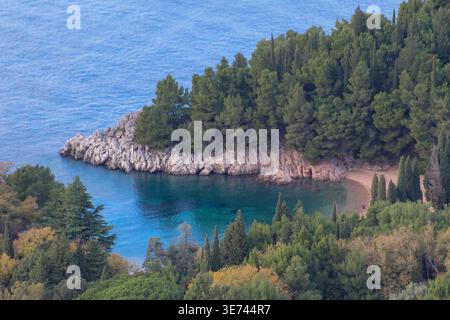 Eine abgeschiedene felsige Bucht mit kristallklarem türkisfarbenem Meer, umgeben von dichtem Kiefernwald und einem kleinen Sandstrand. Stockfoto