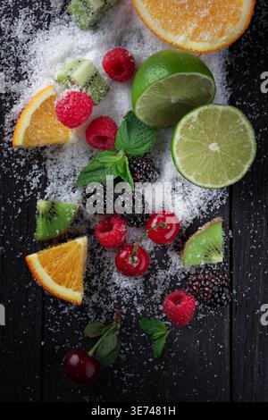 Verschiedene Früchte und Beeren sind kunstvoll auf einer dunklen Holzoberfläche angeordnet, großzügig mit Zuckerkristallen bestreut. Die Komposition verfügt über helle r Stockfoto