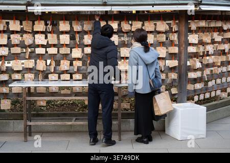 Ein Mann und eine Frau stehen vor einer Mauer, die mit Holzplaketten bedeckt ist, ein beliebter Brauch an japanischen Schreinen und Tempeln Stockfoto