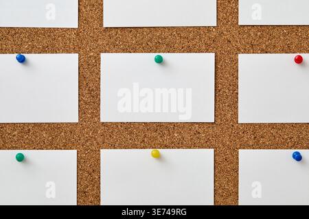 Leere Papierstücke, die mit bunten Stecknadeln an Korkbrett befestigt sind Stockfoto