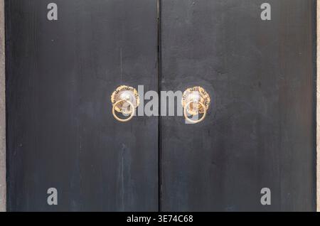 Traditionelle chinesische, schwarze Holztür mit zwei verzierten Messingringklopfern in Shanghai Stockfoto