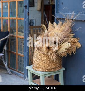 Nahaufnahme von dekorativen getrockneten Blumen und Gras in einem Korb auf einem Holzhocker. Stockfoto
