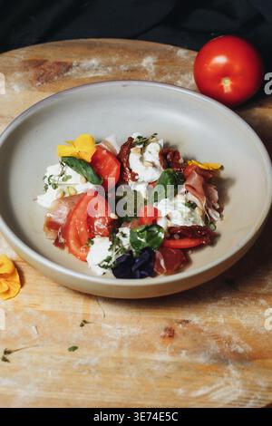 Italienischer Gourmet-Caprese-Salat mit frischem Burrata-Käse-Prosciutto-Schinken, Kirschtomaten und Pesto-Sauce garniert mit essbaren Blumen. Stockfoto