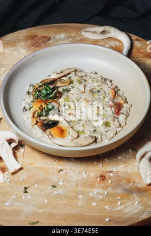 Gourmet-Pilzrisotto mit cremigem Reis, sautierten Stachelpilzen und frischem Mikrogrün, serviert in einer Keramikschale auf einem rustikalen Holzbrett. Stockfoto