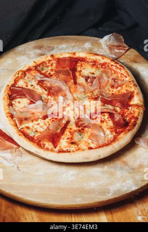 Traditionelle italienische Pinsa romana mit Tomatensauce geschmolzenen Mozzarella Artischockenherzen und dünnen Scheiben Schinken auf einem Holzbrett. Stockfoto