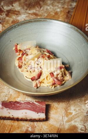 Authentische Pasta Carbonara mit knuspriger Guanciale-cremiger Eiersauce und Parmesanspänen serviert in einer Keramikschale auf rustikalem Hintergrund. Stockfoto