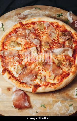 Traditionelle italienische Pinsa romana mit Tomatensauce geschmolzenen Mozzarella Artischockenherzen und dünnen Scheiben Schinken auf einem Holzbrett. Stockfoto