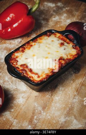 Traditionelle italienische Rinderlasagne mit geschmolzenem Mozzarella in einer schwarzen Keramikplatte auf einem rustikalen bemehlten Holztisch. Stockfoto