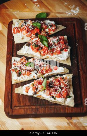 Rustikale italienische Fladenbrotscheiben mit frischer Tomatensalsa, Frischkäse, Parmesan und Basilikumblättern auf einem hölzernen Schneidebrett. Stockfoto