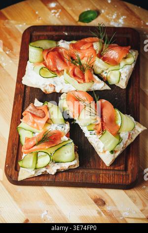 Bruschettas aus geräuchertem Lachs mit frischen Gurkenbändern, Frischkäse und Dill auf einem rustikalen Holzbrett. Stockfoto