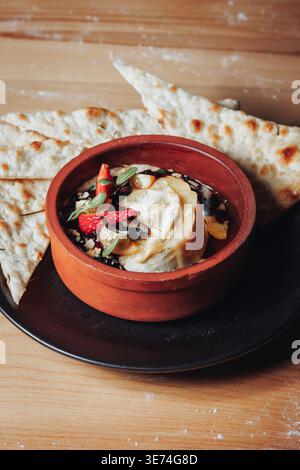 Gourmet-gebackener Camembert-Käse in einem rustikalen Tontopf, serviert mit Fladenbrot und garniert mit frischen Erdbeeren und Beeren. Stockfoto