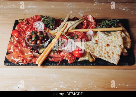 Italienische Gourmet-Wurstplatte mit verschiedenen Salami-Prosciutto-Oliven-Brotstäbchen und Fladenbrot, serviert auf einer Platte aus schwarzem Schiefer. Stockfoto