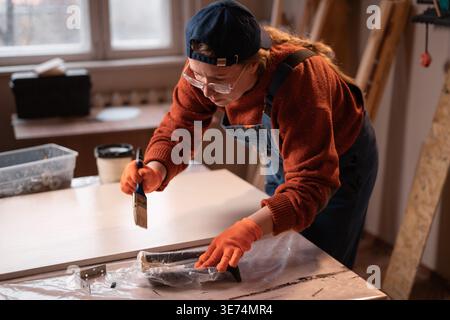 Handwerkskunst und Heimwerkerarbeit in Handarbeit. Zimmermanninnen tragen blaue Overalls und tragen Malmöbel mit Pinsel in Zimmereien auf Stockfoto