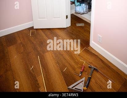Pinkfarbene Wände umgeben den Raum. Weiße Türständer sind offen. Die Installation von Holzböden wird fortgesetzt. Werkzeuge und Sägemehl bedecken den Boden. Hier ist eine Renovierung zu Hause dargestellt Stockfoto
