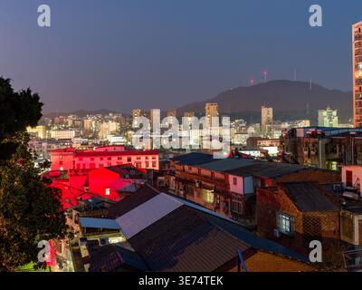 Ein weicher Blick bei Nacht auf ein dicht besiedeltes Stadttal mit traditionellen Dächern, die unter roter Beleuchtung leuchten und von modernen Stadtlichtern unterlegt werden Stockfoto