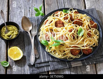Pasta alla Polpette, Teller italienischer Pasta Linguine mit frittierten Fleischbällchen, frischen Basilikumblättern, Zitronen- und Pesto-Sauce auf grauer Serviette mit Löffel und für Stockfoto