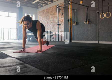 Erwachsene Frau in schwarzem Oberteil und Shorts, die Bergsteiger auf roter Matte in der Nähe von Ringen, Kopierraum. Fitnessstudio, Workout, Training, Fitness, Studio, naturalli Stockfoto