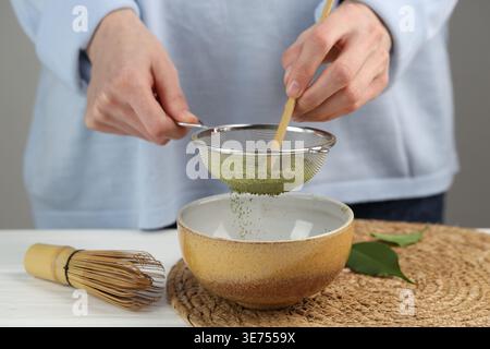 Frau, die Matcha-Pulver in eine Schüssel am weißen Tisch siebt, Nahaufnahme Stockfoto