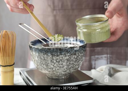 Frau, die Matcha-Pulver in eine Schüssel am weißen Tisch siebt, Nahaufnahme Stockfoto