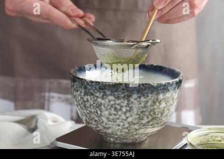 Frau, die Matcha-Pulver in eine Schüssel am Tisch siebt, Nahaufnahme Stockfoto
