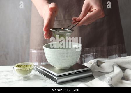 Frau, die Matcha-Pulver in eine Schüssel am weißen Tisch siebt, Nahaufnahme Stockfoto