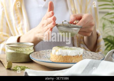 Frau siebt Matcha-Pulver auf Meringue-Tarte am Holztisch, Nahaufnahme Stockfoto