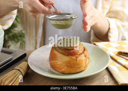 Frau siebt Matcha-Pulver auf Zimtrolle am Holztisch, Nahaufnahme Stockfoto