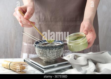 Frau, die Matcha-Pulver in eine Schüssel am weißen Tisch siebt, Nahaufnahme Stockfoto