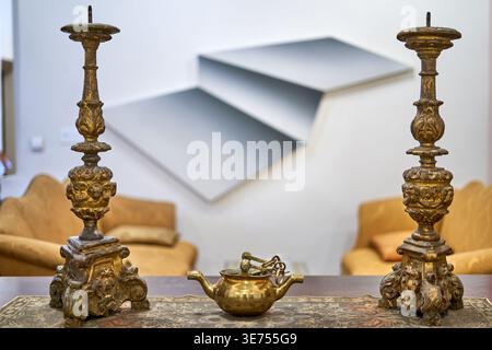 Eine Nahaufnahme-Stillleben mit zwei kunstvollen antiken Kerzenständern mit gealterter Goldpatina und aufwendigen barocken Schnitzereien, die eine kleine Messing-Teekanne flankieren Stockfoto
